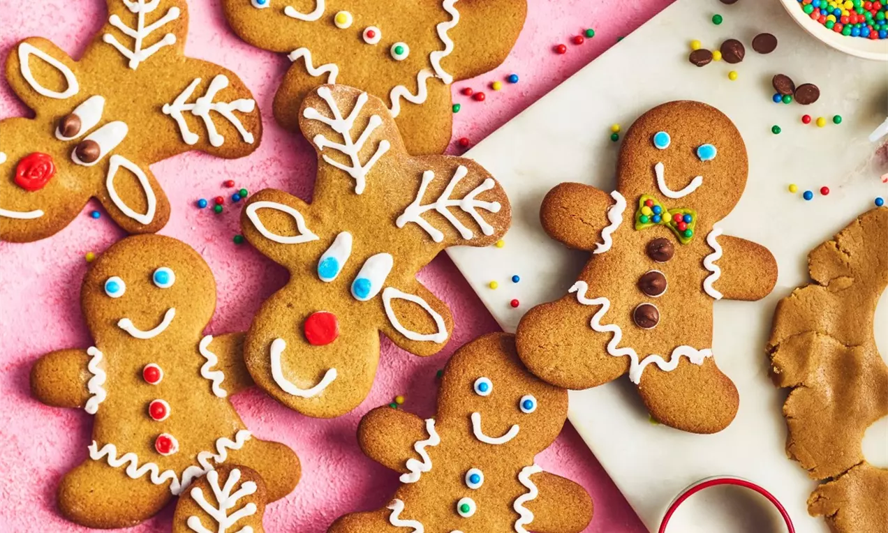 Biscuits de pain d'épices brun doré en forme de bonhommes et de rennes décorés de glaçage blanc et de perles colorées sur fond rose
