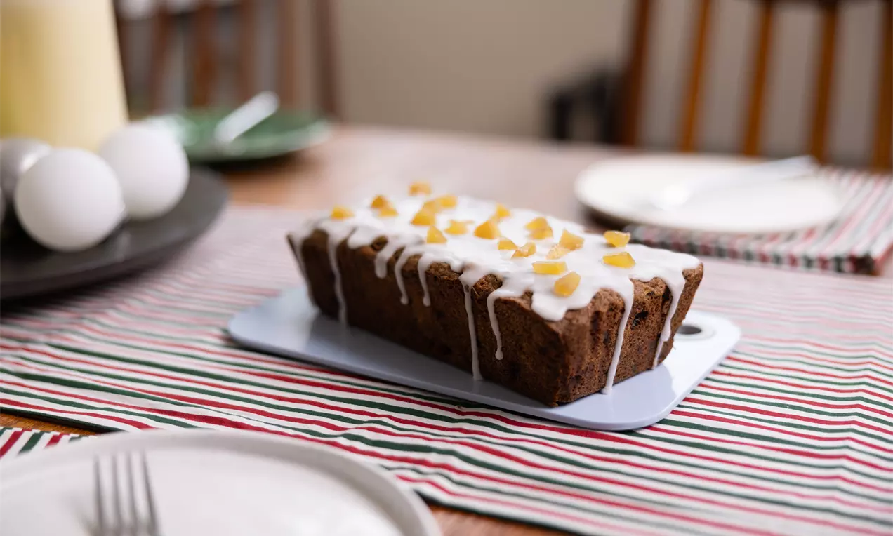 Cake rectangulaire brun moelleux parsemé de pépites de chocolat, nappé de glaçage blanc et décoré de morceaux de fruits jaunes opalescents