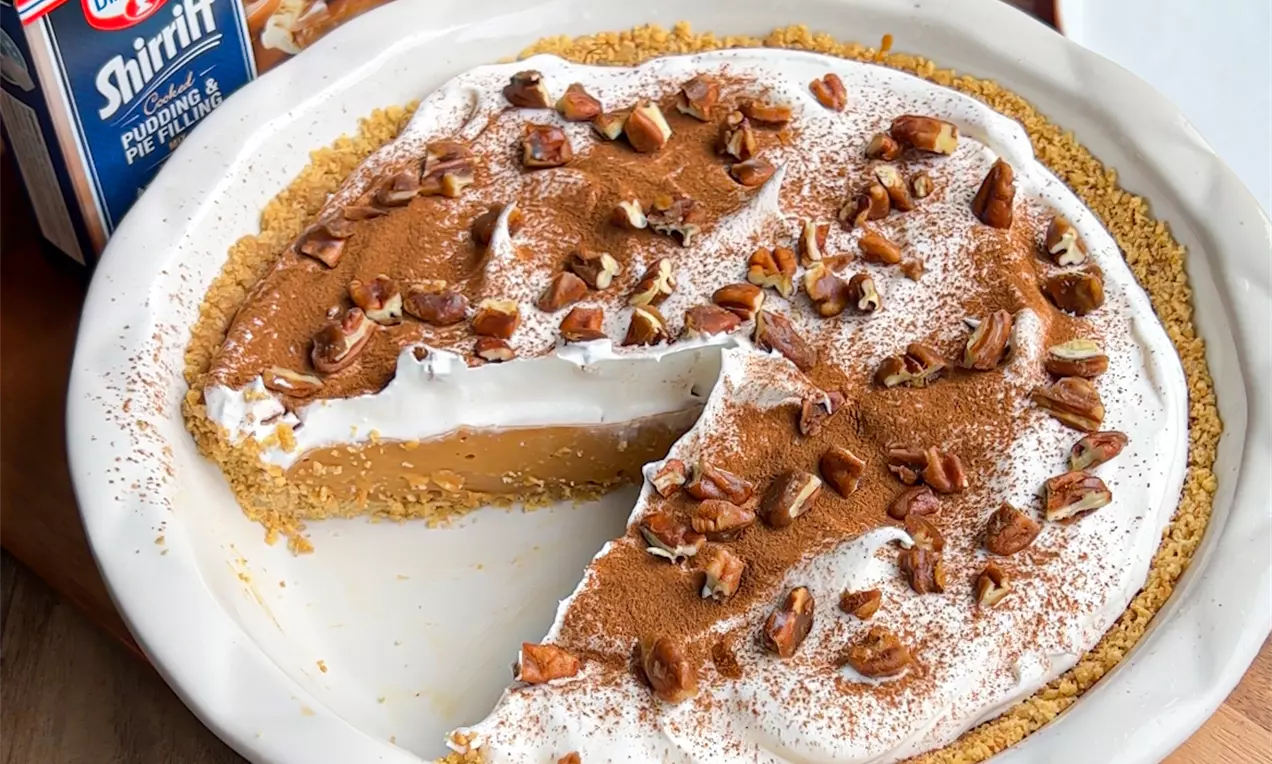 Tarte ronde dans un moule blanc, garnie de crème fouettée, saupoudrée de cannelle et de noix croquantes sur une croûte dorée