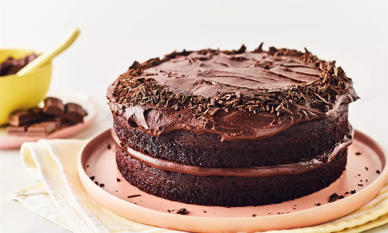 Gâteau au chocolat végétalien à deux étages avec glaçage brillant, copeaux de chocolat en couronne sur le dessus, posé sur une assiette rose
