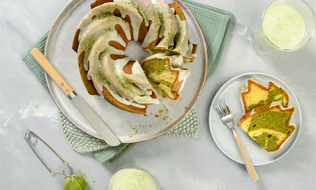 Gâteau Bundt moelleux en spirale bicolore matcha et vanille, glaçage blanc et saupoudrage vert sur une assiette ronde avec des tranches à côté