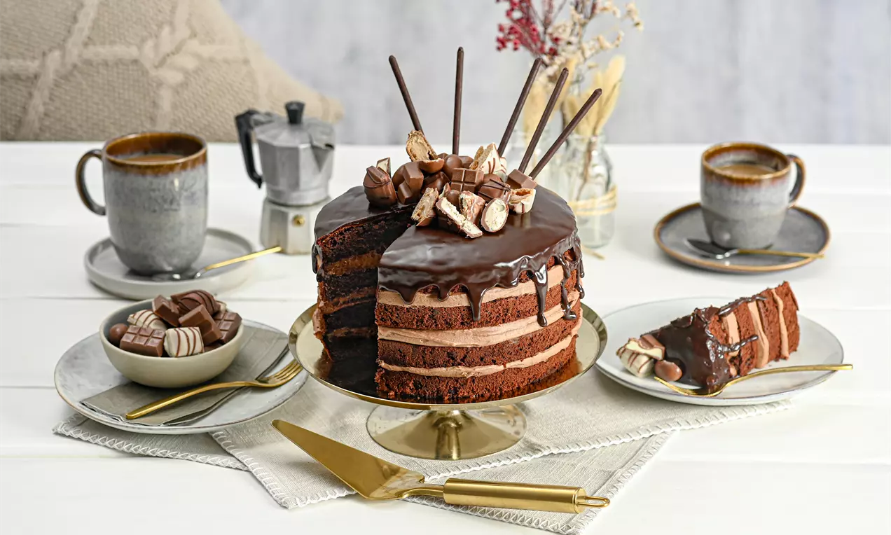 Gâteau au chocolat en couches riches, glaçage brillant, garni de biscuits et bâtonnets chocolatés, présenté sur un plat doré avec une tranche servie